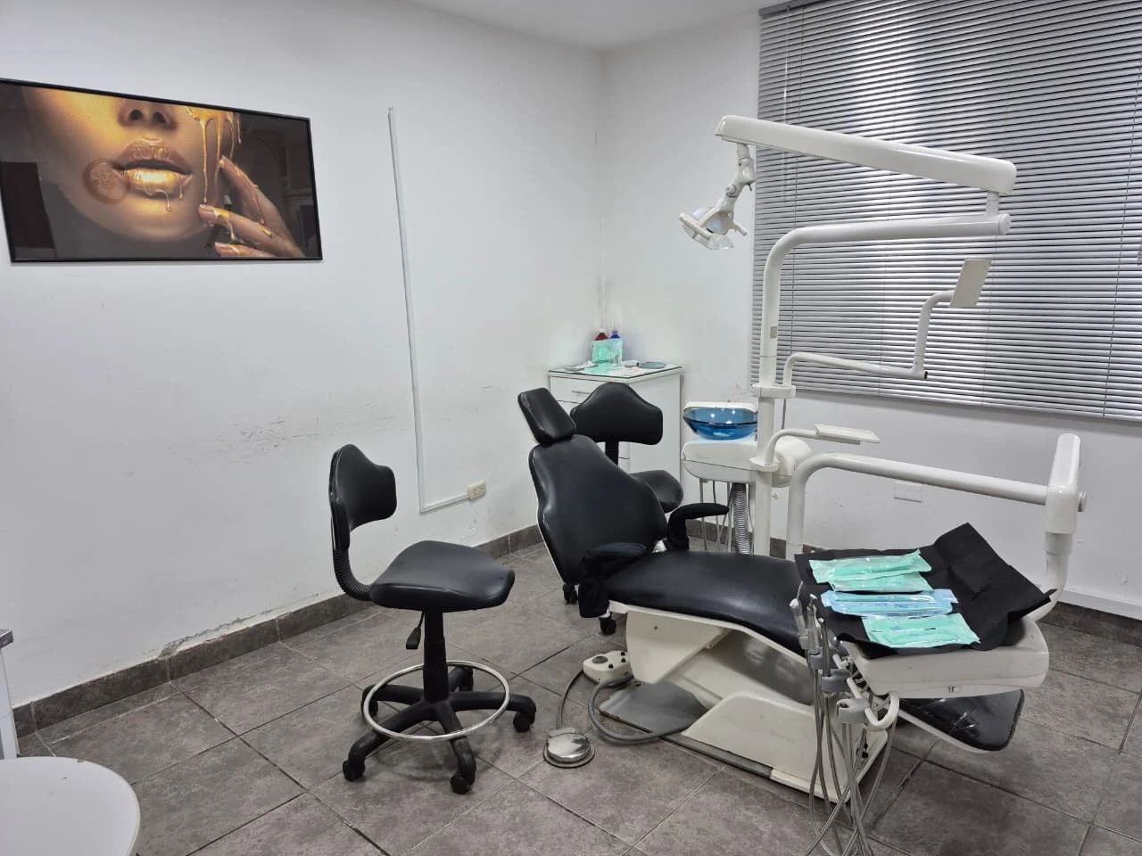 El consultorio de cirugía, implantes y endodoncia, con el sillón dental negro preparado con campos y bolsas de instrumental esterilizado