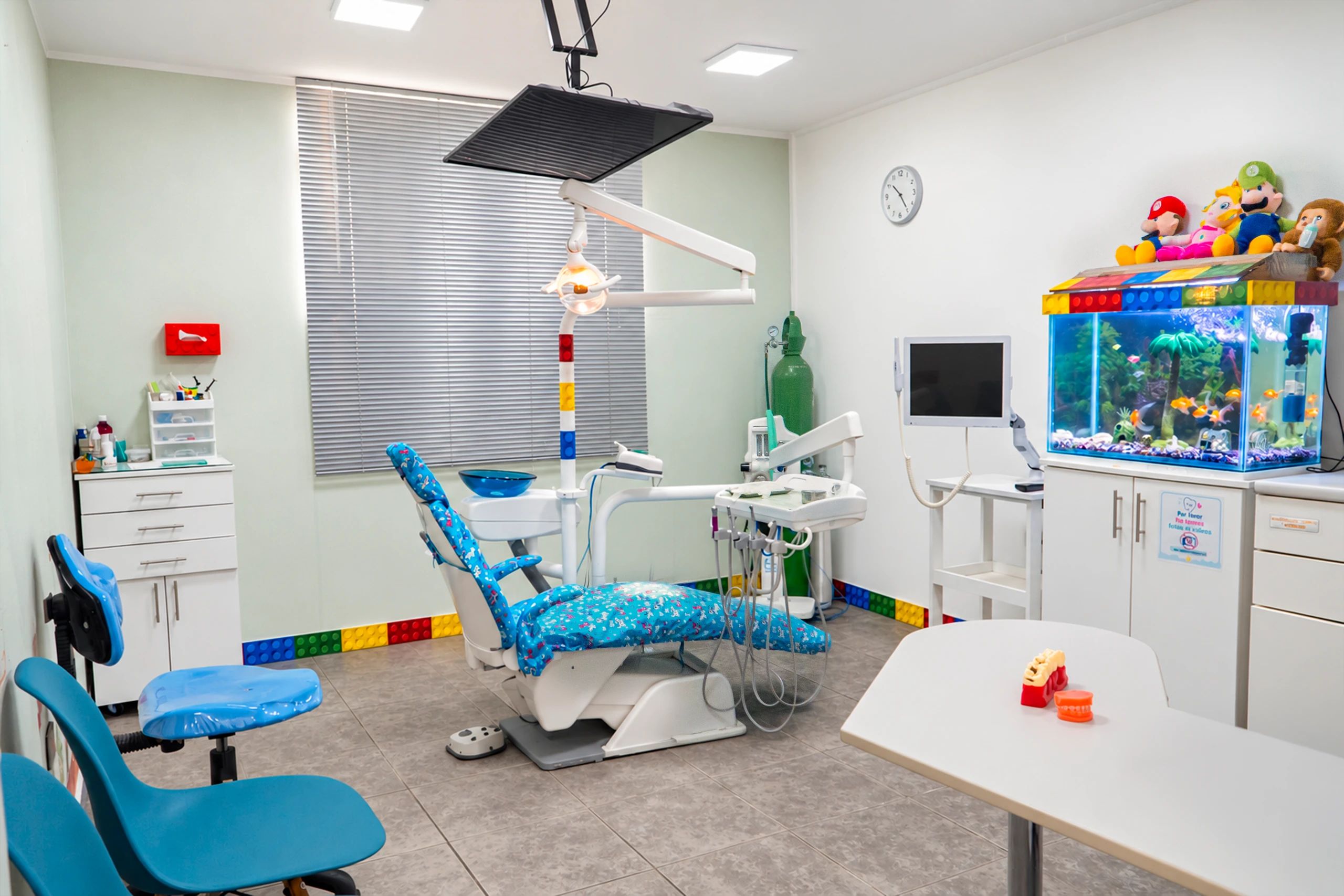 El consultorio infantil completo, con el sillón tapizado de estampado azul, una pecera con peluches encima y un zócalo de bloques de colores