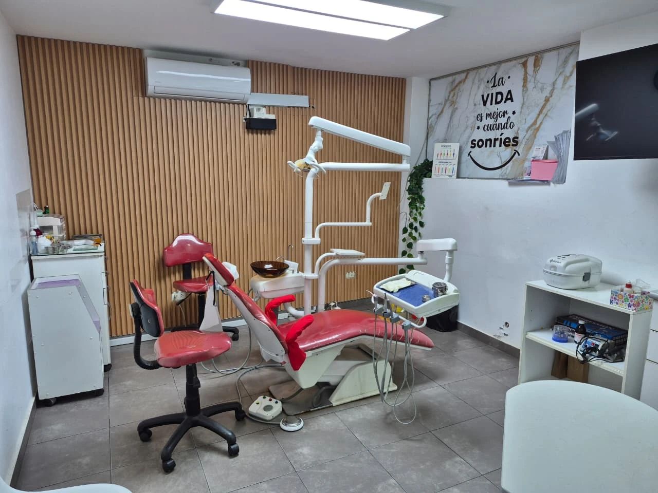 El consultorio de rehabilitación, con el sillón dental rojo frente a la pared revestida en madera y un cuadro que dice La vida es mejor cuando sonríes